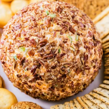 A festive holiday cheese ball served with crackers and fresh herbs as decoration.