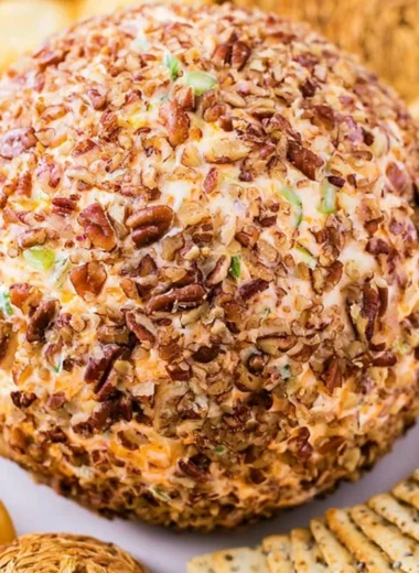 A festive holiday cheese ball served with crackers and fresh herbs as decoration.