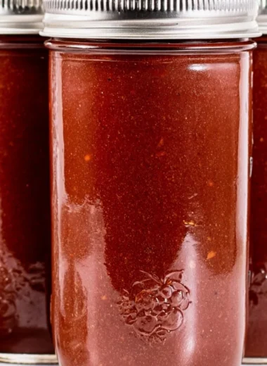 Jar of homemade BBQ sauce with fresh ingredients on a wooden table